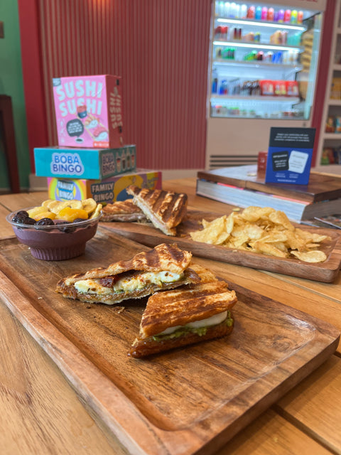 Sandwiches on a wooden board with snacks and drinks in the background