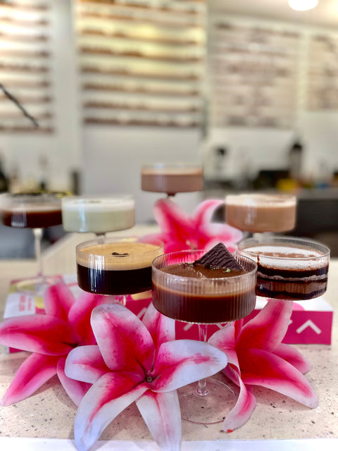 Small glasses with dark liquid on a table with pink flowers and a blurred background